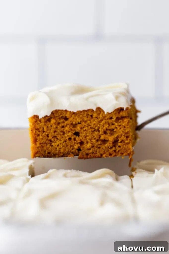 A single piece of pumpkin cake with cream cheese frosting being removed from the baking dish, showing distinct cake and frosting layers.