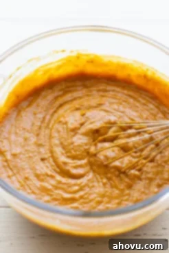 A glass mixing bowl filled with smooth, orange pumpkin cake batter, ready for baking.