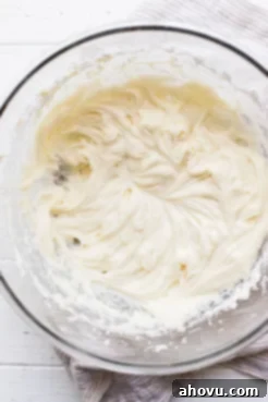 A clear glass mixing bowl filled with creamy, smooth cream cheese frosting, ready to be spread.