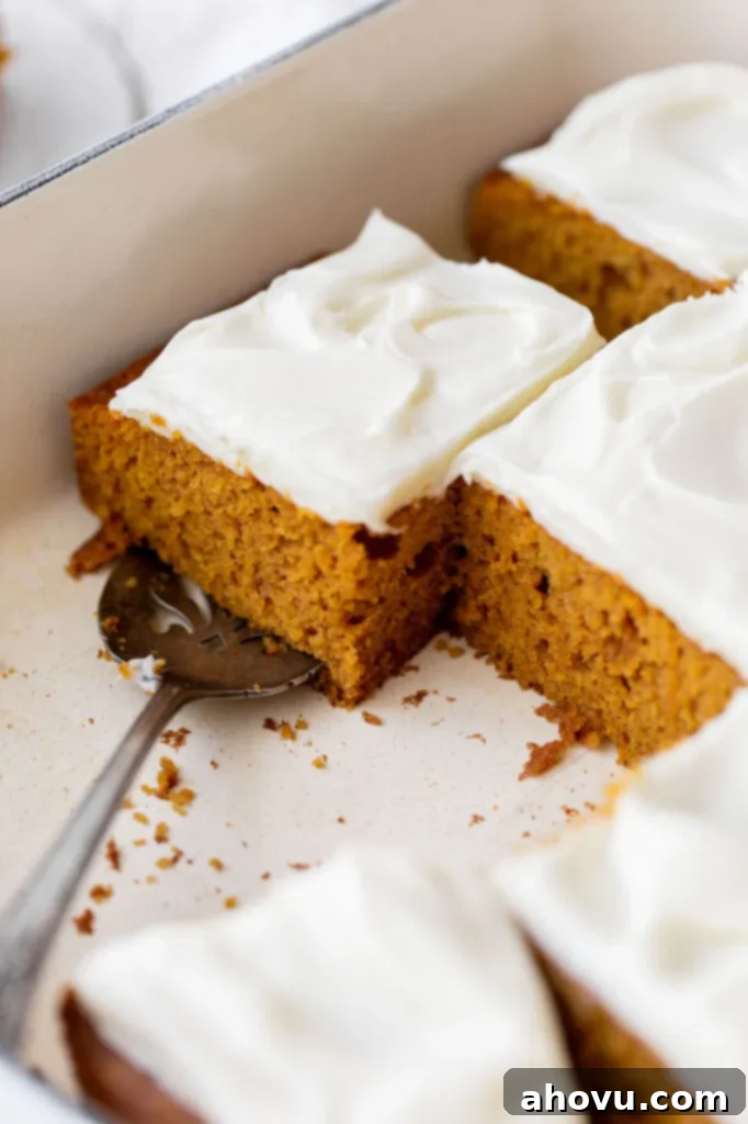 A 9x13 inch baking dish containing a fully frosted pumpkin cake with several square pieces already removed, showing the cake's interior.