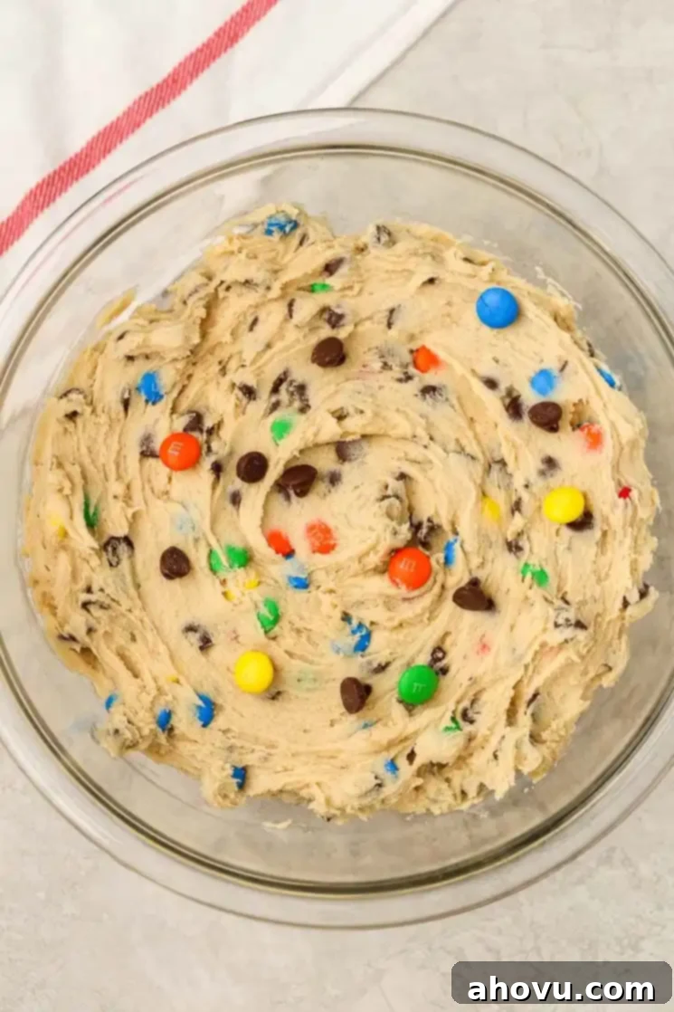 Glass mixing bowl filled with cookie dough that's studded with M&M's and chocolate chips. 