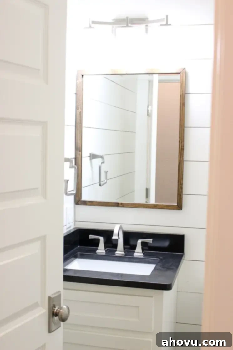 A chic half bathroom featuring striking white shiplap walls and elegant black countertops, blending modern and rustic elements.