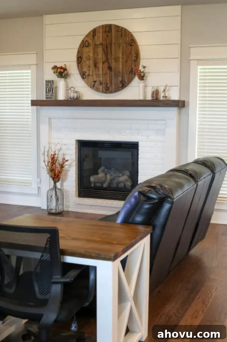 A spacious living room with a white fireplace, large windows, and a farmhouse-style desk, showcasing a blend of comfort and functionality.