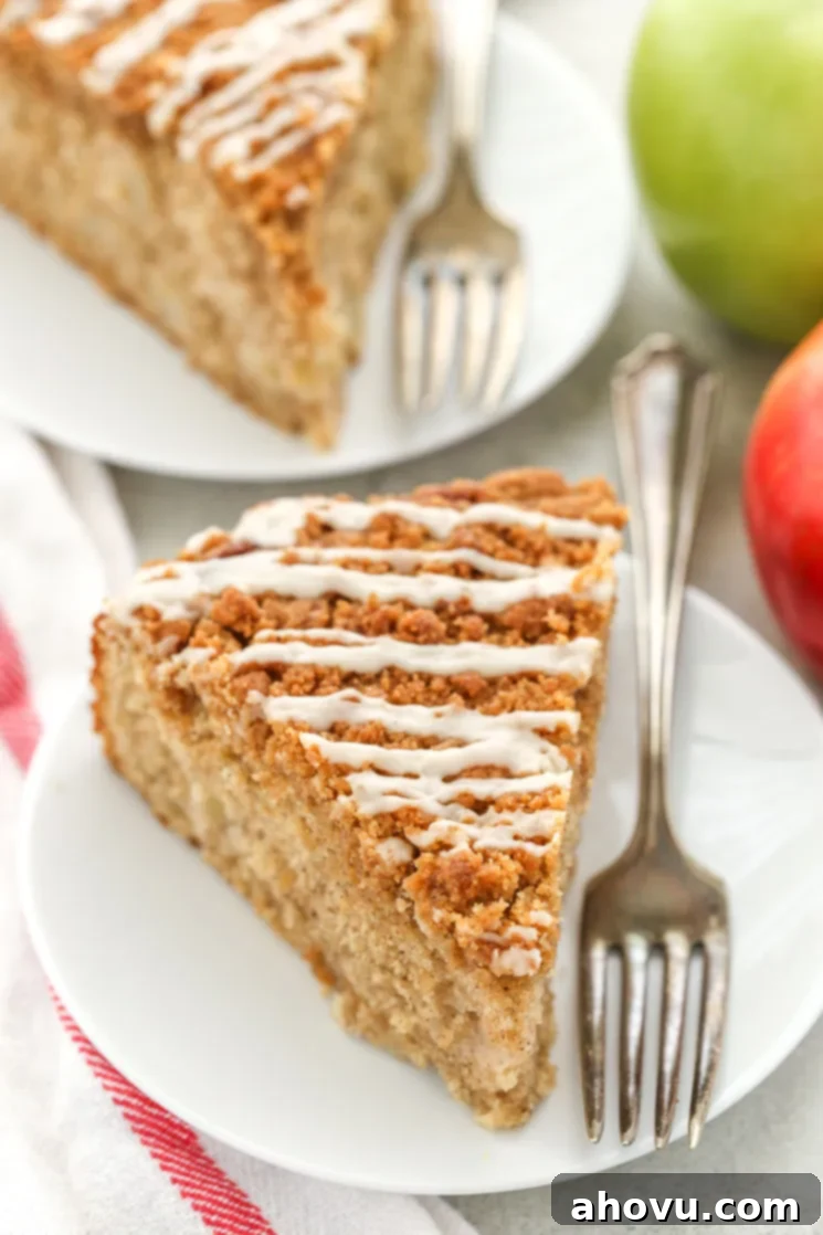 Two slices of apple coffee cake on white plates with forks. 