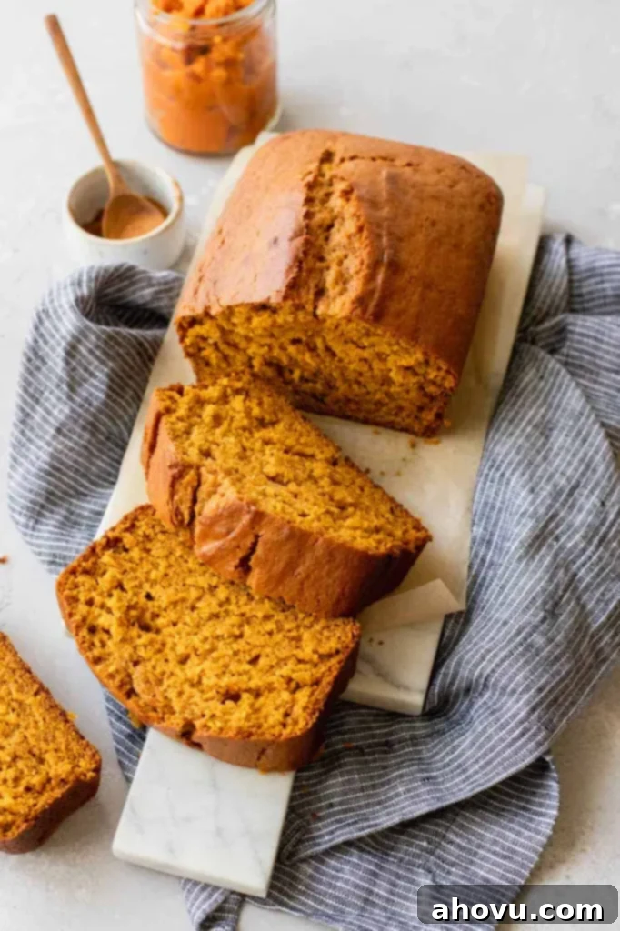 A beautifully sliced loaf of classic pumpkin bread, showing its moist texture, arranged on a elegant marble serving tray.