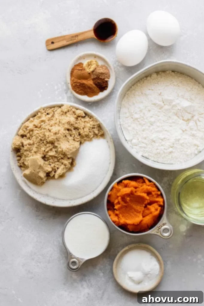 Various ingredients for baking pumpkin bread, including flour, spices, pumpkin puree, sugars, and wet ingredients, displayed in bowls on a rustic gray surface.