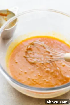 The wet ingredients for pumpkin bread, including pumpkin puree, sugars, oil, buttermilk, eggs, and vanilla extract, thoroughly mixed in a clear glass bowl.