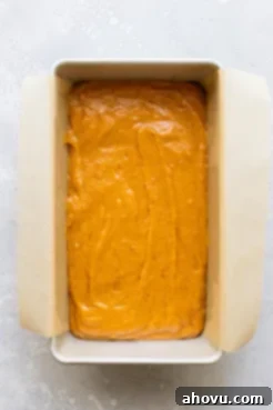An overhead view of smooth pumpkin bread batter evenly spread in a parchment-lined loaf pan, ready for the oven.