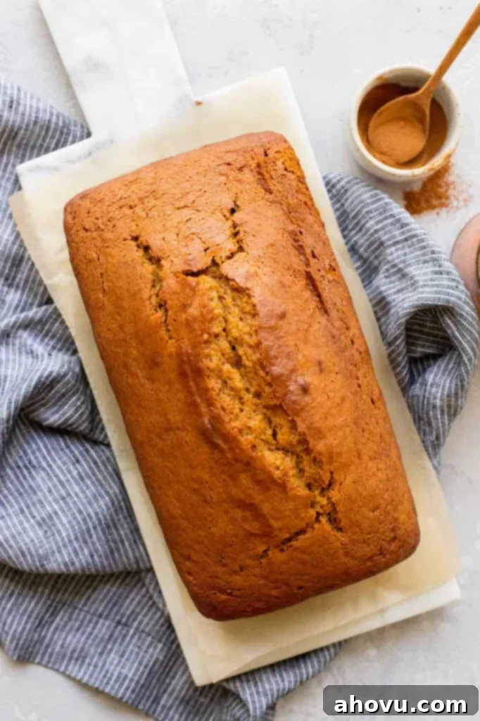 A freshly baked loaf of pumpkin bread cooling on a pristine marble serving tray, with a bowl of cinnamon sticks in the soft-focus background, evoking a cozy fall atmosphere.
