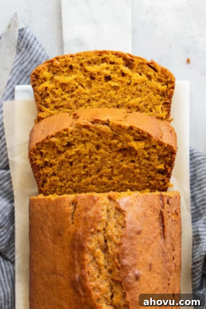 An overhead view of a classic pumpkin bread loaf that has been expertly sliced, showcasing its wonderfully moist, tender, and spiced texture.