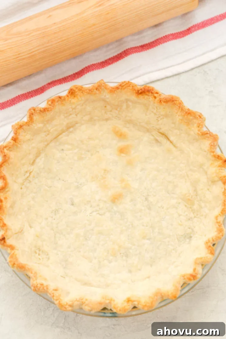A partially baked pie crust next to a wood rolling pin on a striped towel. 
