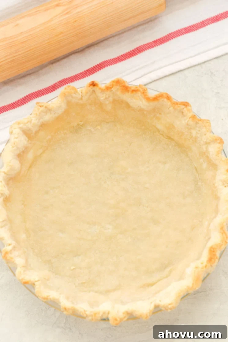 A partially baked pie crust next to a striped towel and rolling pin.