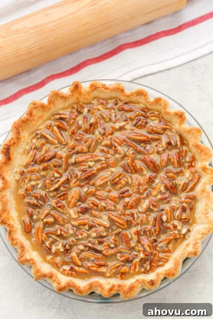 Overhead view of a pecan pie next to a rolling pin and a striped towel. 