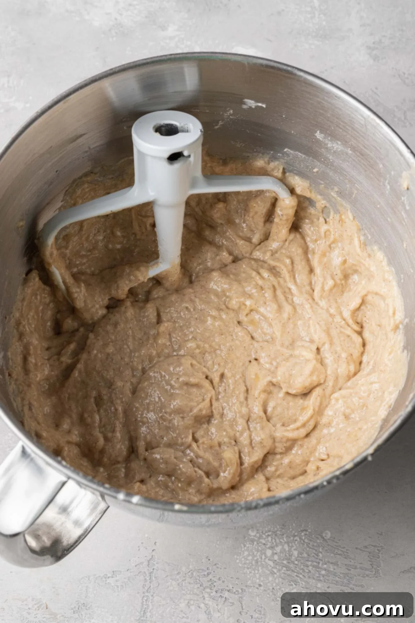 An overhead view of fluffy banana bread batter in a mixing bowl, ready for the cinnamon swirl, with a paddle attachment from a stand mixer.
