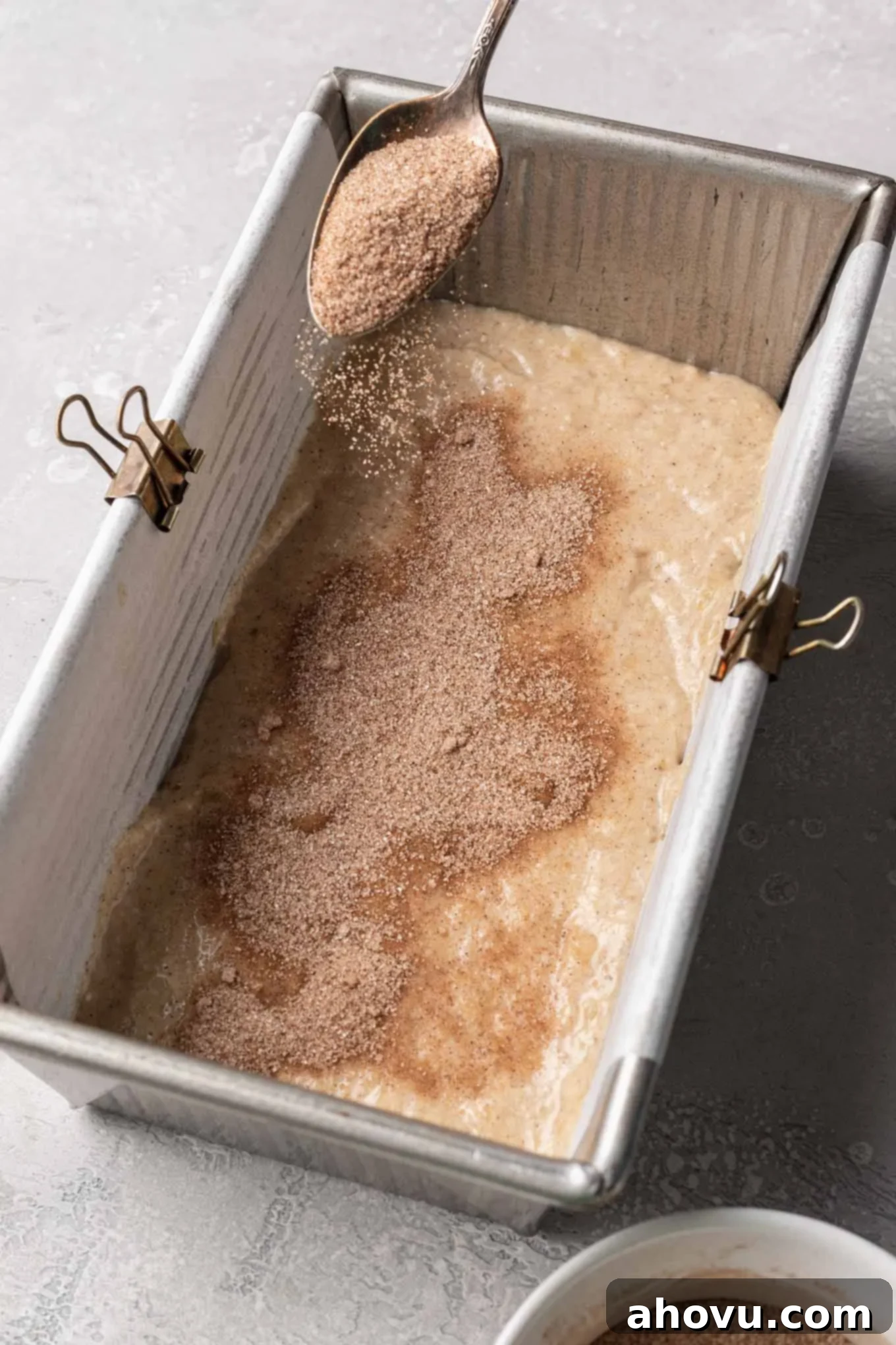 Banana bread batter in a loaf pan with a generous layer of cinnamon and sugar sprinkled on top, creating the first swirl layer.