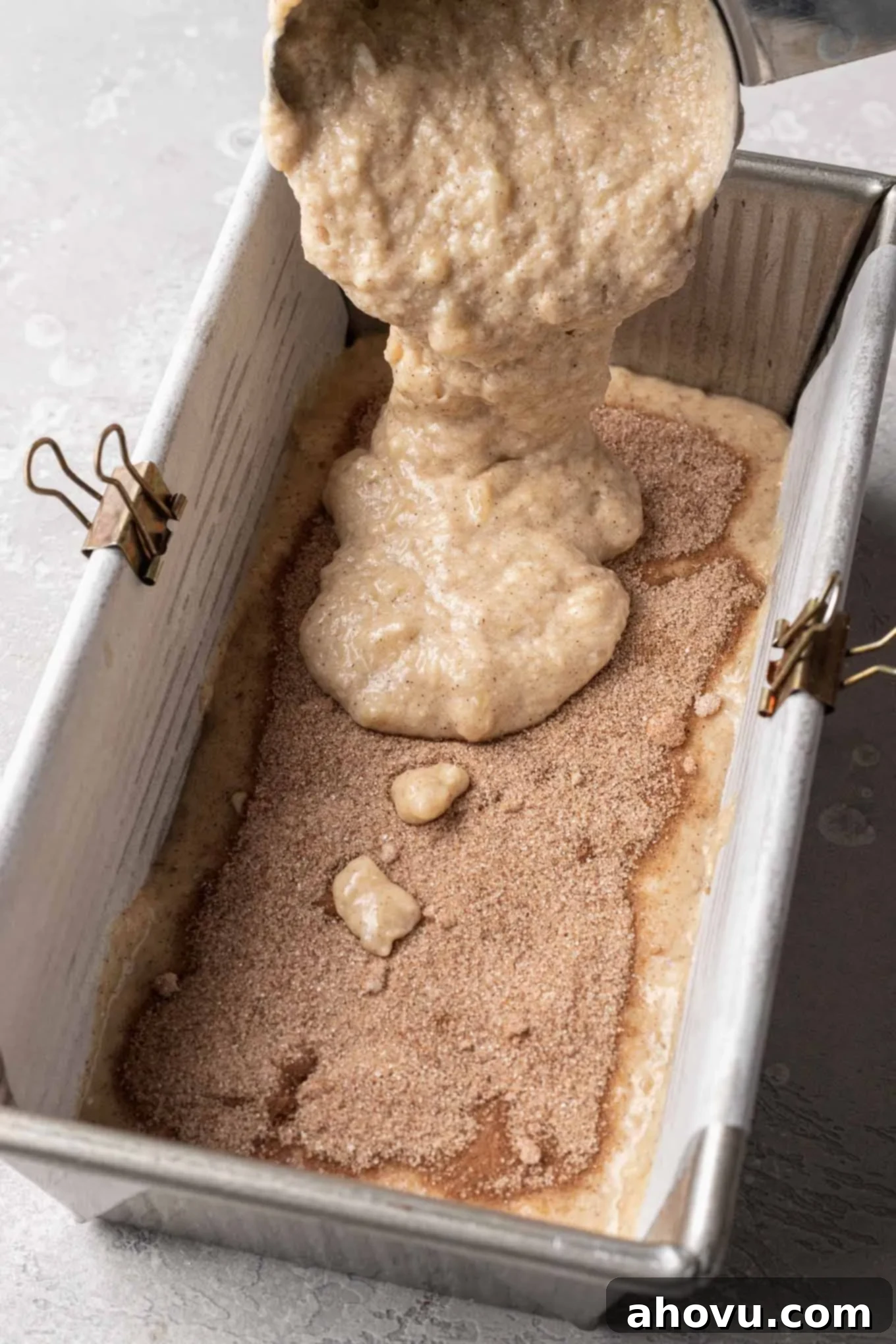 More banana bread batter being carefully added on top of the cinnamon sugar filling, completing the layered swirl.