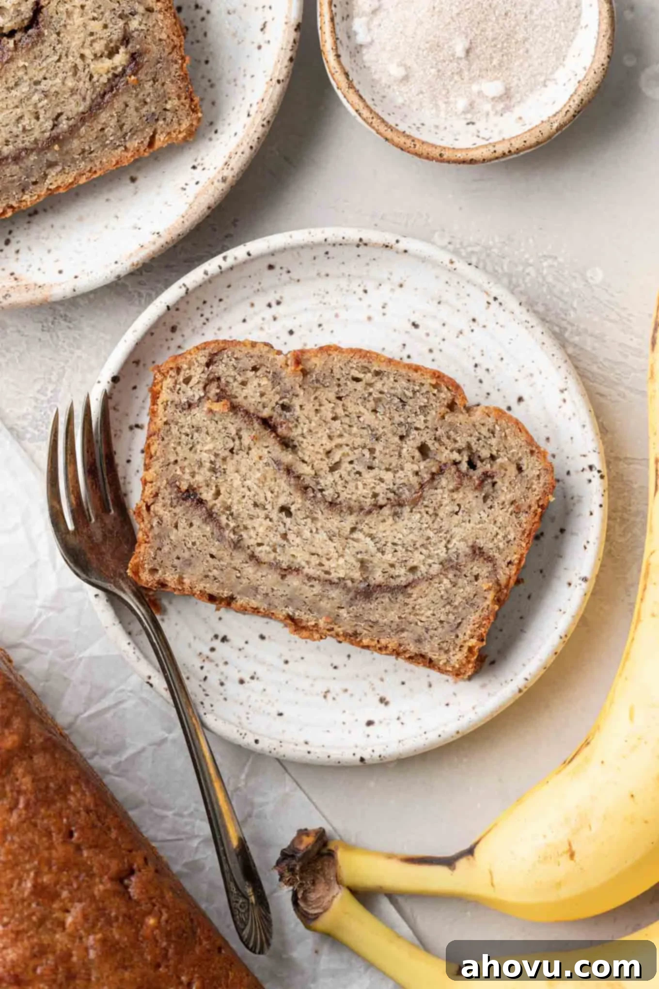 An overhead view of a perfectly sliced piece of banana cinnamon bread on a dessert plate, with a fork ready to enjoy.