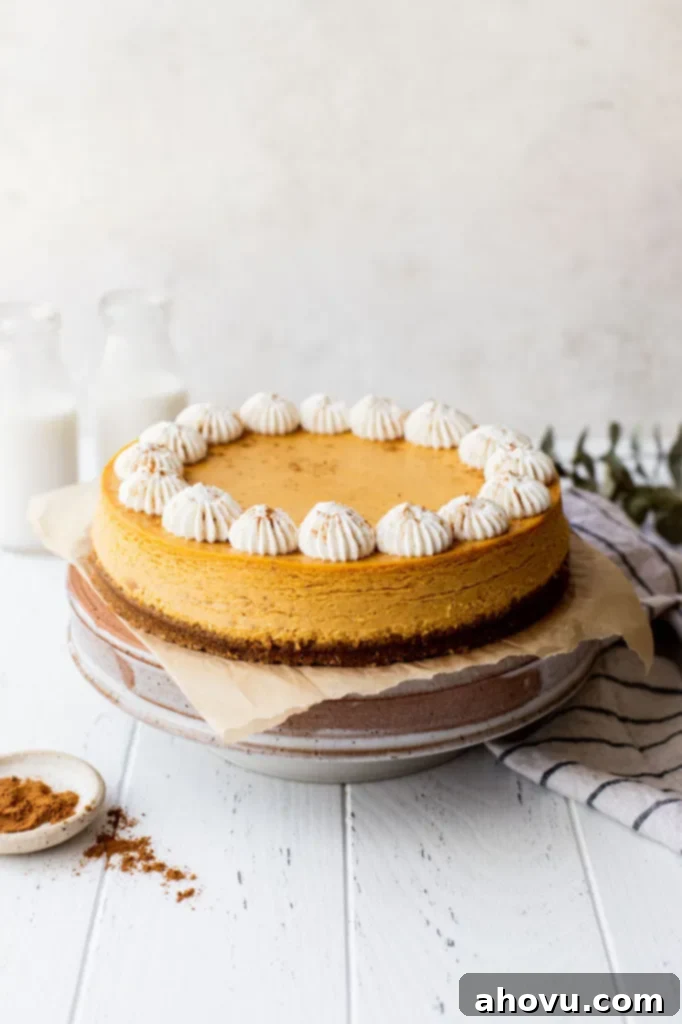 A whole pumpkin cheesecake on a elegant cake stand, surrounded by festive cinnamon sticks and a glass of milk, capturing the essence of a cozy autumn treat.