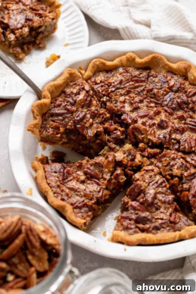 A beautifully baked classic pecan pie in a white ceramic dish, with one slice carefully removed to showcase its rich, amber filling and crunchy pecan topping.