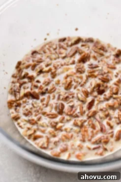 A clear glass mixing bowl filled with the rich, amber pecan pie filling, showcasing the chopped pecans suspended within the sweet mixture.