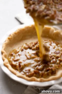 Rich pecan pie filling being carefully poured from a glass bowl into a perfectly blind-baked pie crust in a white dish, ready for baking.
