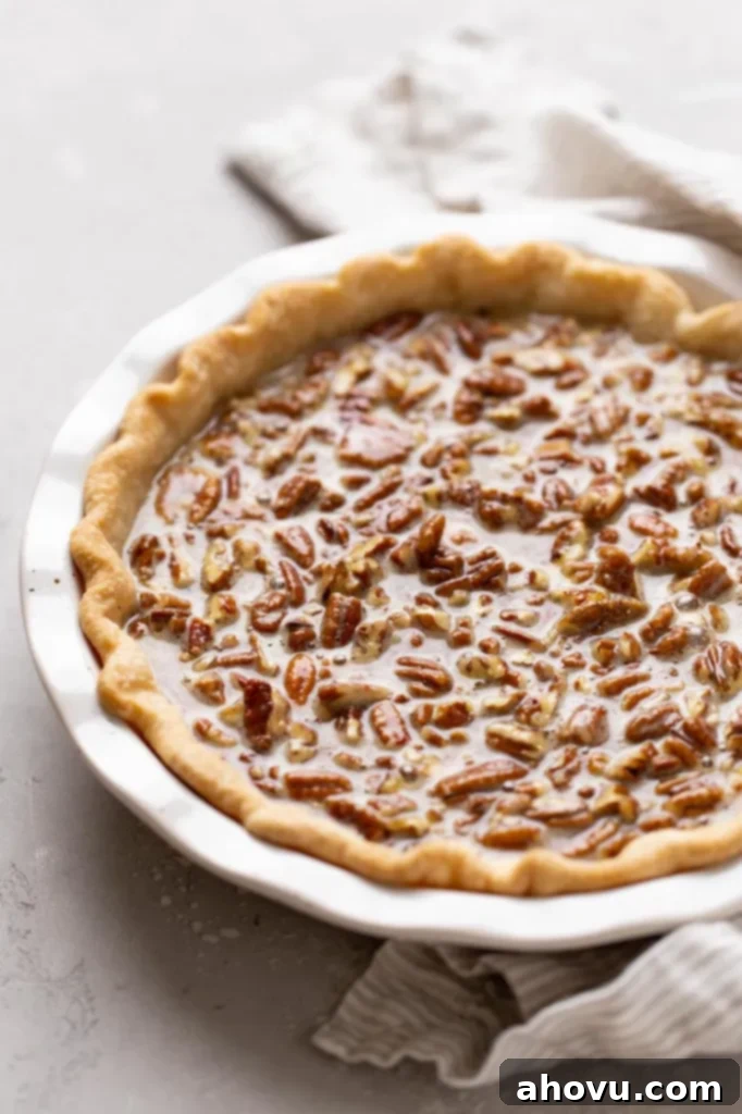 A partially assembled pecan pie in a white baking dish, topped with foil on the crust edges, ready to be placed in the oven for baking.