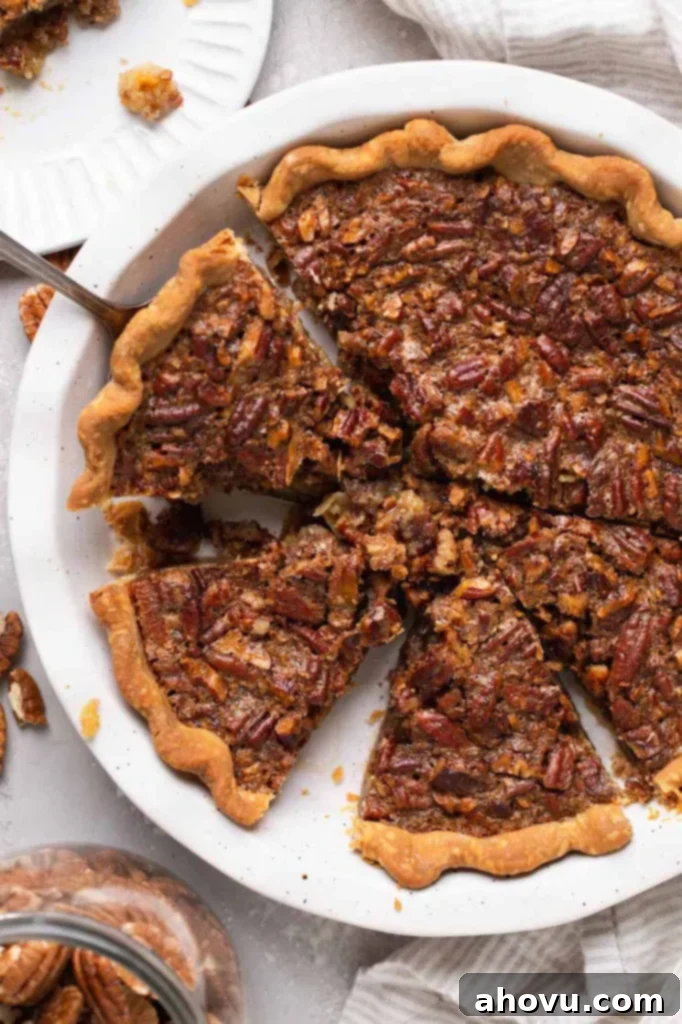An overhead shot of a freshly baked pecan pie in a white ceramic dish, perfectly sliced into wedges, highlighting its golden crust and rich, glistening filling.