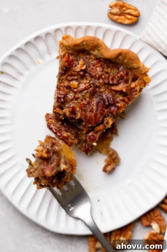 A single, perfectly portioned slice of pecan pie on a white plate, with a fork gently taking a bite, showing the rich texture of the filling and crisp crust.