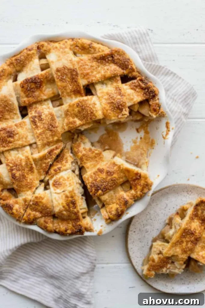 A beautifully baked apple pie in a white pie dish with one slice expertly removed and placed on a white plate, ready to be enjoyed.