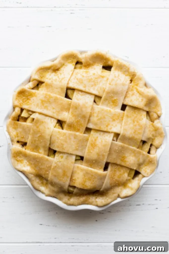 A freshly assembled apple pie, adorned with a delicate lattice crust and sparkling coarse sugar, poised and ready to be placed into the preheated oven for baking.