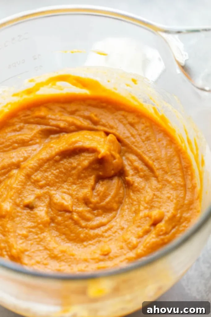 A close-up shot of creamy, mashed sweet potatoes in a large glass mixing bowl.