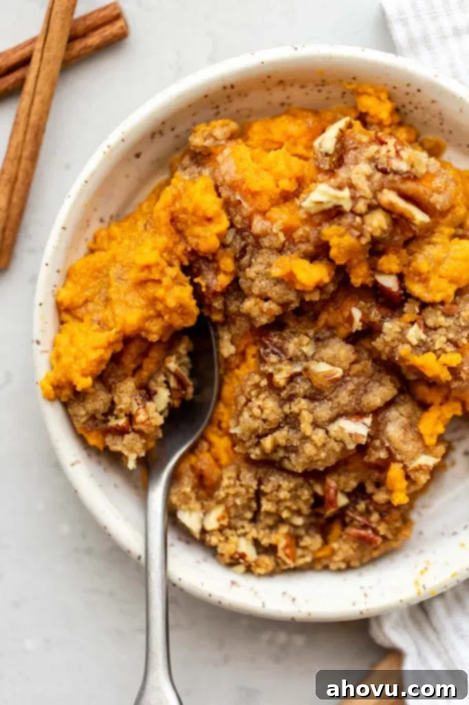 An individual serving of sweet potato casserole, topped with streusel, in a white speckled bowl.