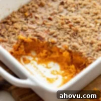 A sweet potato casserole in a baking dish with one corner scooped out to show the sweet potato base.