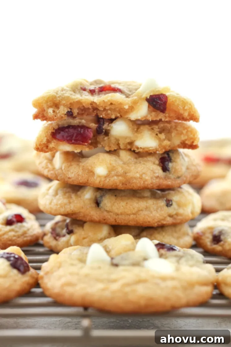 A close-up of a stack of freshly baked, soft white chocolate cranberry cookies, showing their thick, chewy texture and abundant mix-ins, perfect for holiday baking.