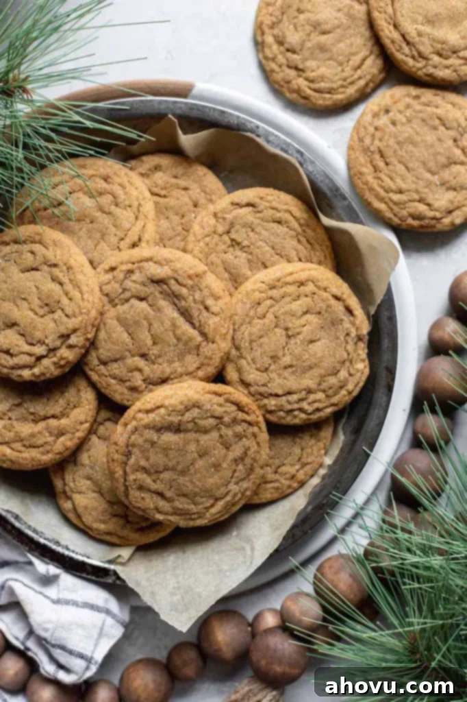 A round baking pan filled with golden-brown molasses cookies, beautifully arranged and surrounded by rustic Christmas decorations like pinecones, berries, and festive greenery, creating a warm, inviting holiday scene.