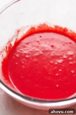 Close-up of vibrant red velvet cupcake batter swirling in a clear glass mixing bowl, ready for baking.