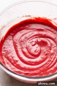 A second view of the rich, deep red red velvet cupcake batter in a glass bowl, showcasing its smooth texture.