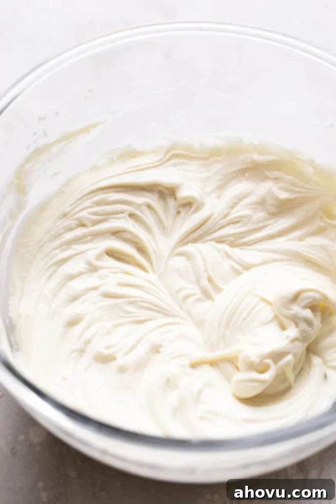 Velvety Red Delights 4 Close-up overhead shot of perfectly smooth and creamy cream cheese frosting in a clear glass mixing bowl, ready to be piped onto cooled cupcakes.