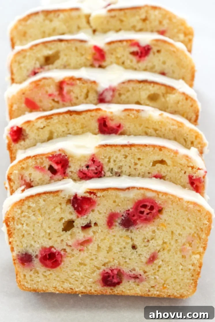 Six perfectly sliced pieces of moist cranberry orange bread, stacked invitingly on a wooden board. Each slice beautifully showcases the vibrant red cranberries embedded within the rich, golden crumb, indicating its tender texture.