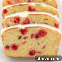 A loaf of freshly baked cranberry orange bread, perfectly glazed and sliced, displayed on a piece of parchment paper, ready to be enjoyed.