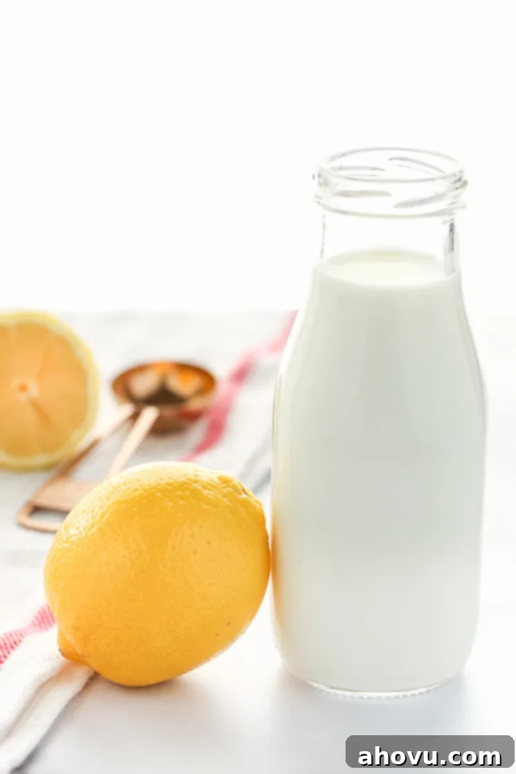 An image of a clear glass measuring cup filled with milk and a lemon beside it. A white napkin, copper measuring spoon, and sliced lemon in the background, illustrating the simplicity of the ingredients.