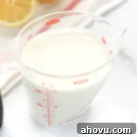 A clear measuring cup filled with homemade buttermilk along with a white napkin and lemons in the background.