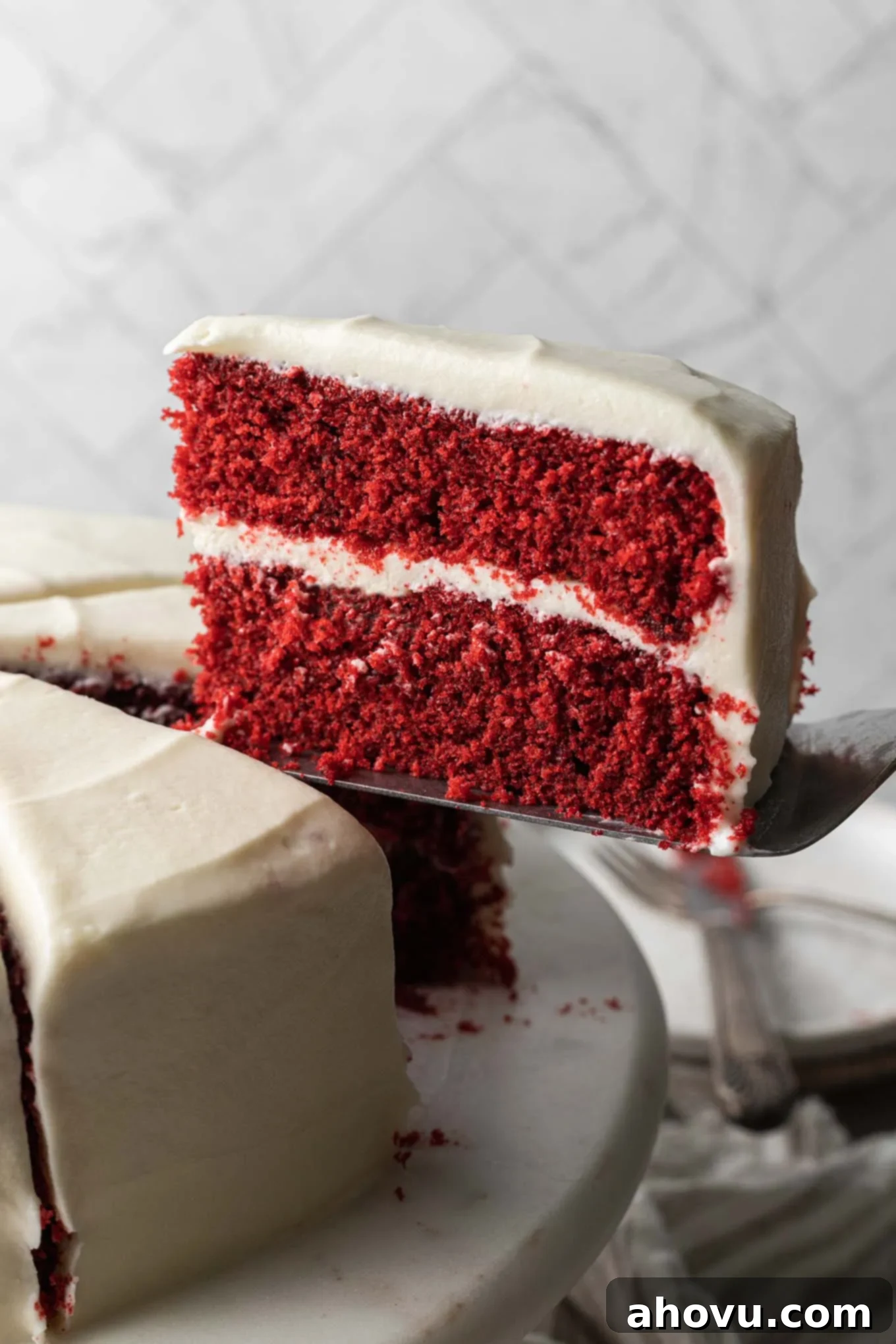 A slice of red velvet cake being served from a cake stand. 