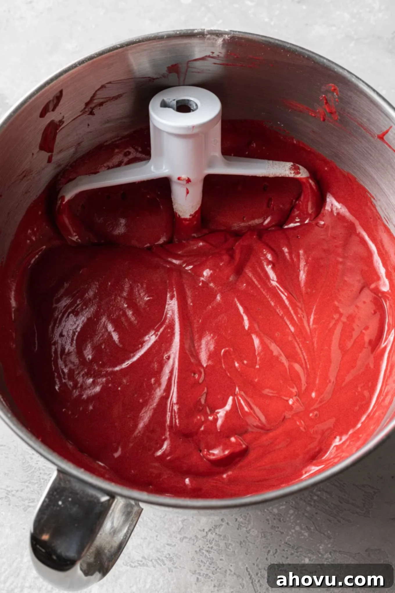An overhead view of red velvet cake batter in a mixing bowl with a paddle attachment.
