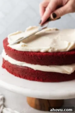 A red velvet layer cake on a cake stand in the process of being frosted.