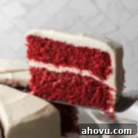 A sliced red velvet cake on a cake stand. The slice of cake is being lifted up to show the texture of the cake.
