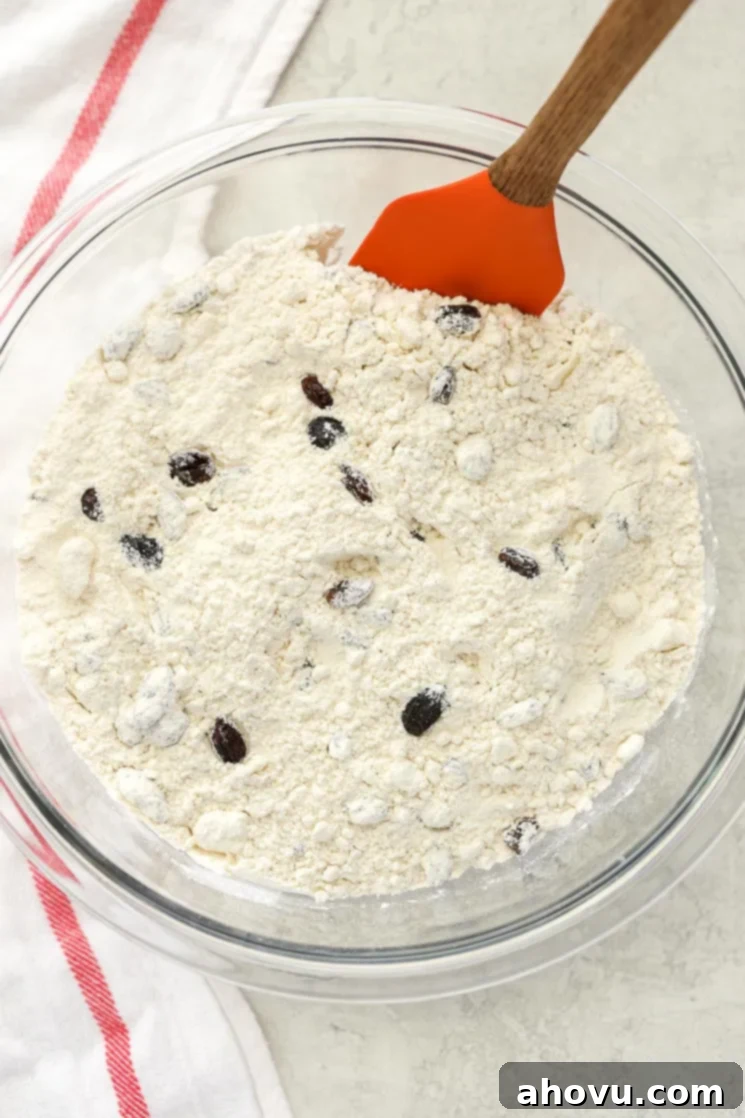 A clear glass bowl filled with the dry ingredients for Irish Soda Bread sitting on top of a white and red napkin. 