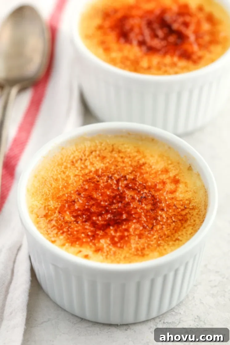 Two white ramekins filled with homemade crème brûlée and a white napkin and two spoons on the side.