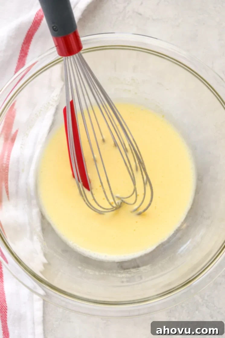 A clear glass bowl filled with egg yolks whisked with sugar and a white napkin on the side.
