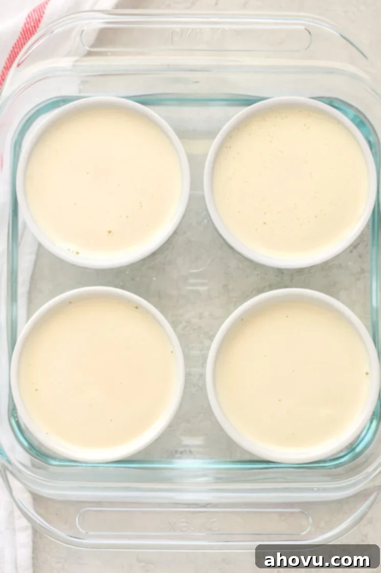 An 8-inch square glass baking dish with four white ramekins filled with the crème brûlée and water inside the dish.